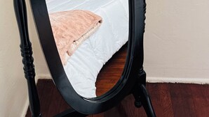 Cama com cabeceira escura, roupa de cama branca e um cobertor rosa.