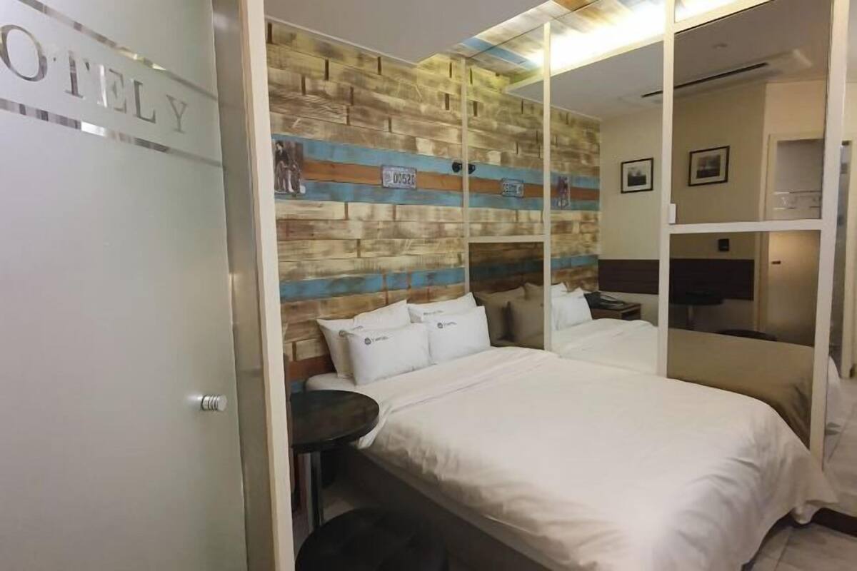 Een hotelkamer met een bed, een klein rond tafeltje, een wand met een houten paneeldecor en een deur met een geëtste ruit.