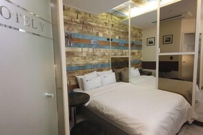 A hotel room with a bed, a small round table, a wall with a wooden panel design, and a door with a frosted glass panel. - Eunpyeong Y Hotel (Seoul)