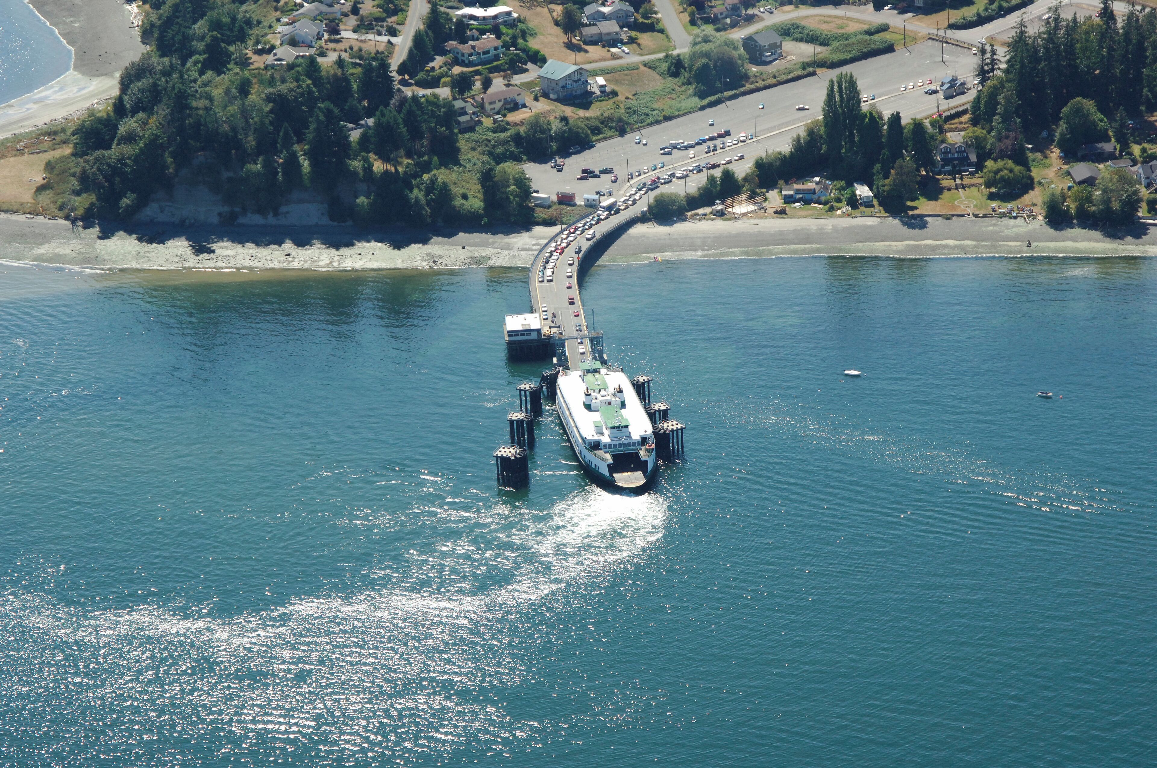 Vue aérienne d’un ferry amarré à un quai, avec une route menant à un quartier résidentiel.