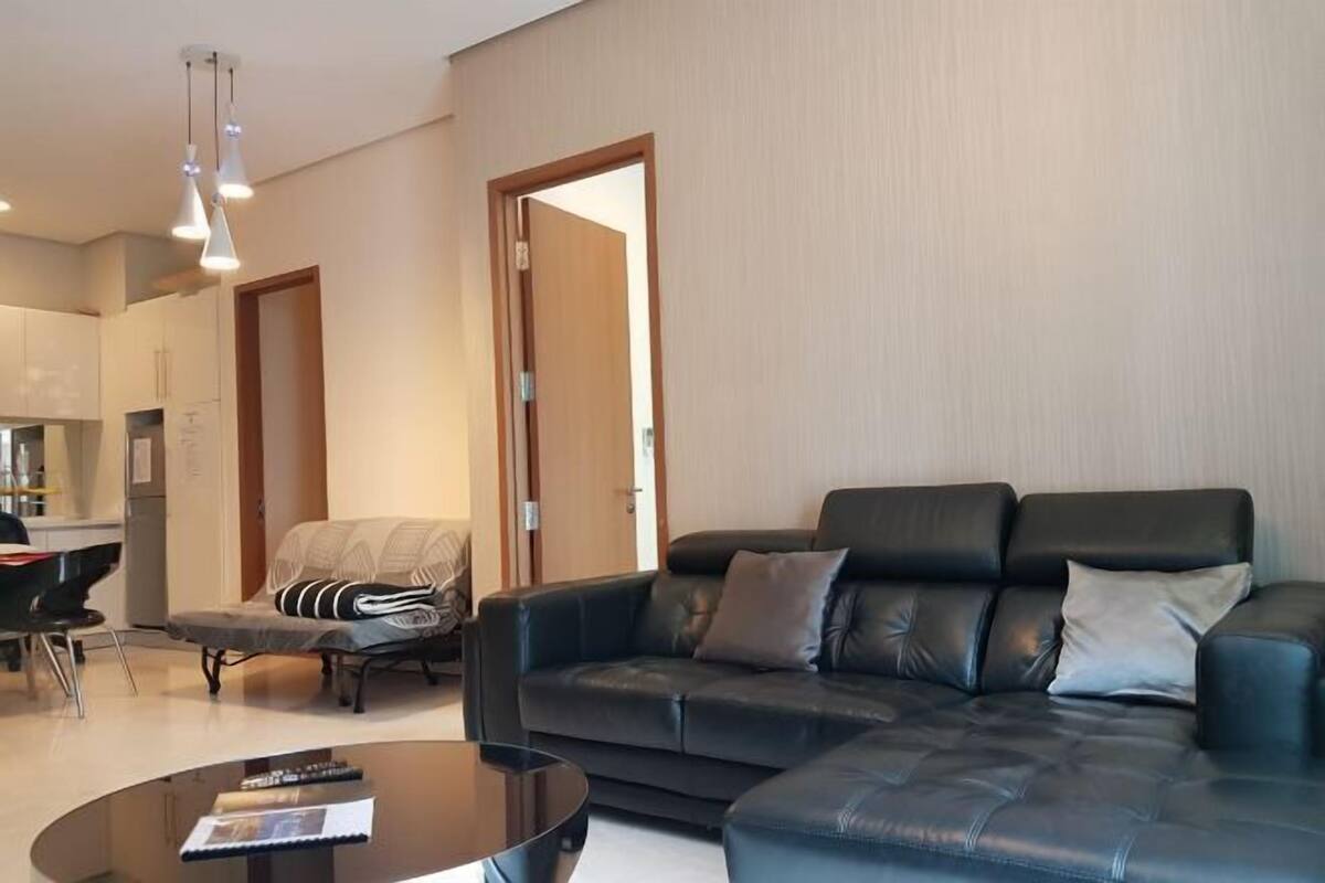 Un salon moderne avec un canapé en cuir noir, une table basse en verre et un coin repas comprenant une chaise et une table.