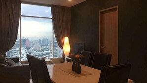 A modern hotel room with a large window, a dining table with chairs, a lamp, and a city view. - Soho Suites @ KLCC by Luxury Suites Asia (Kuala Lumpur)