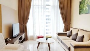 A modern hotel room with a sofa, a coffee table, a TV, and a large window with curtains. - Soho Suites @ KLCC by Luxury Suites Asia (Kuala Lumpur)