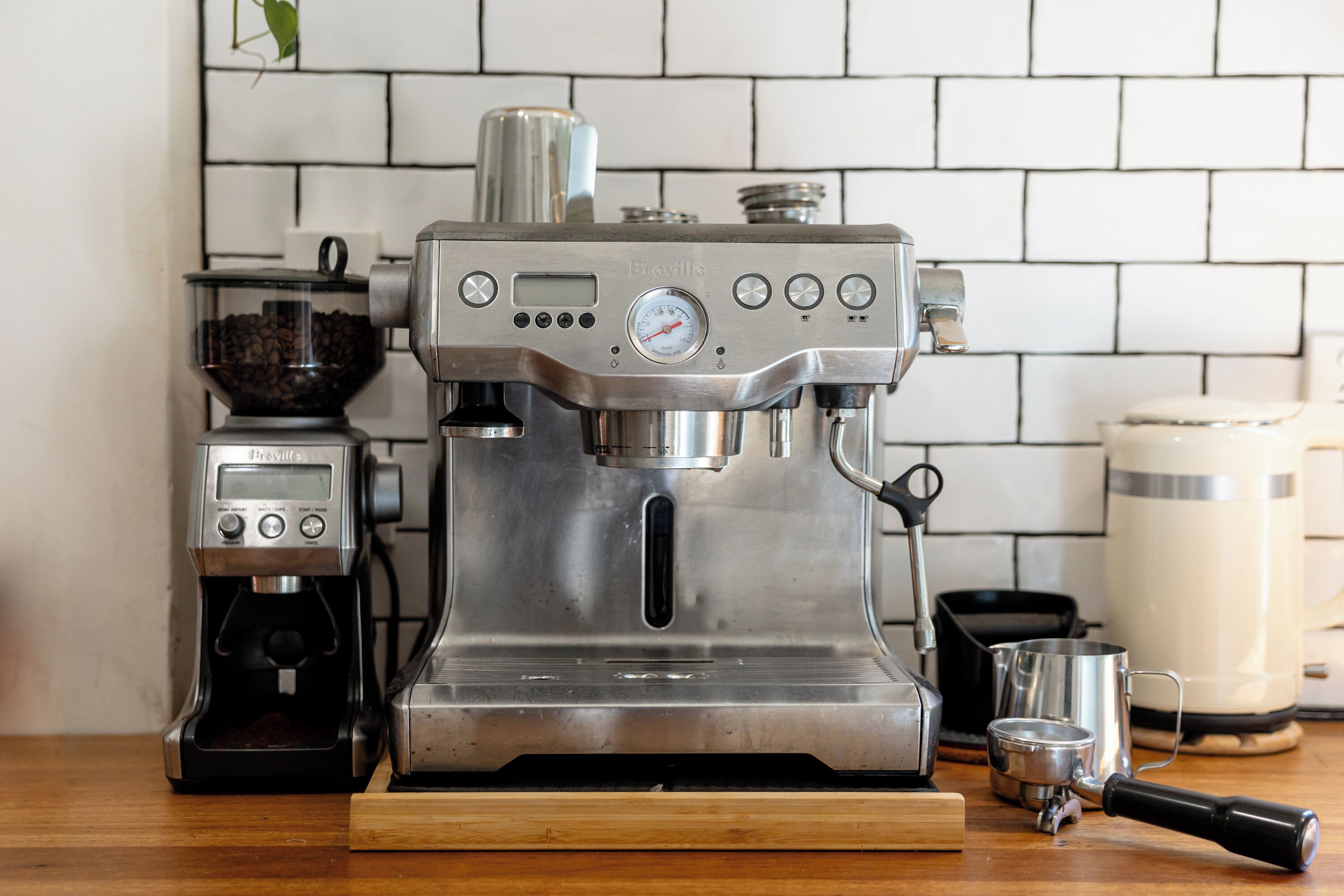 Een Breville espressomachine op een keukentafel, samen met een koffiemolen, een melkopschuimer en een koffiezetapparaat.
