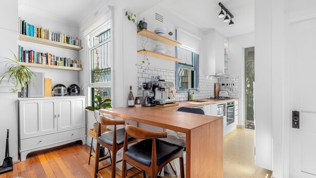 Een moderne keuken met houten barstoelen, witte kastjes en een inbouweiland.