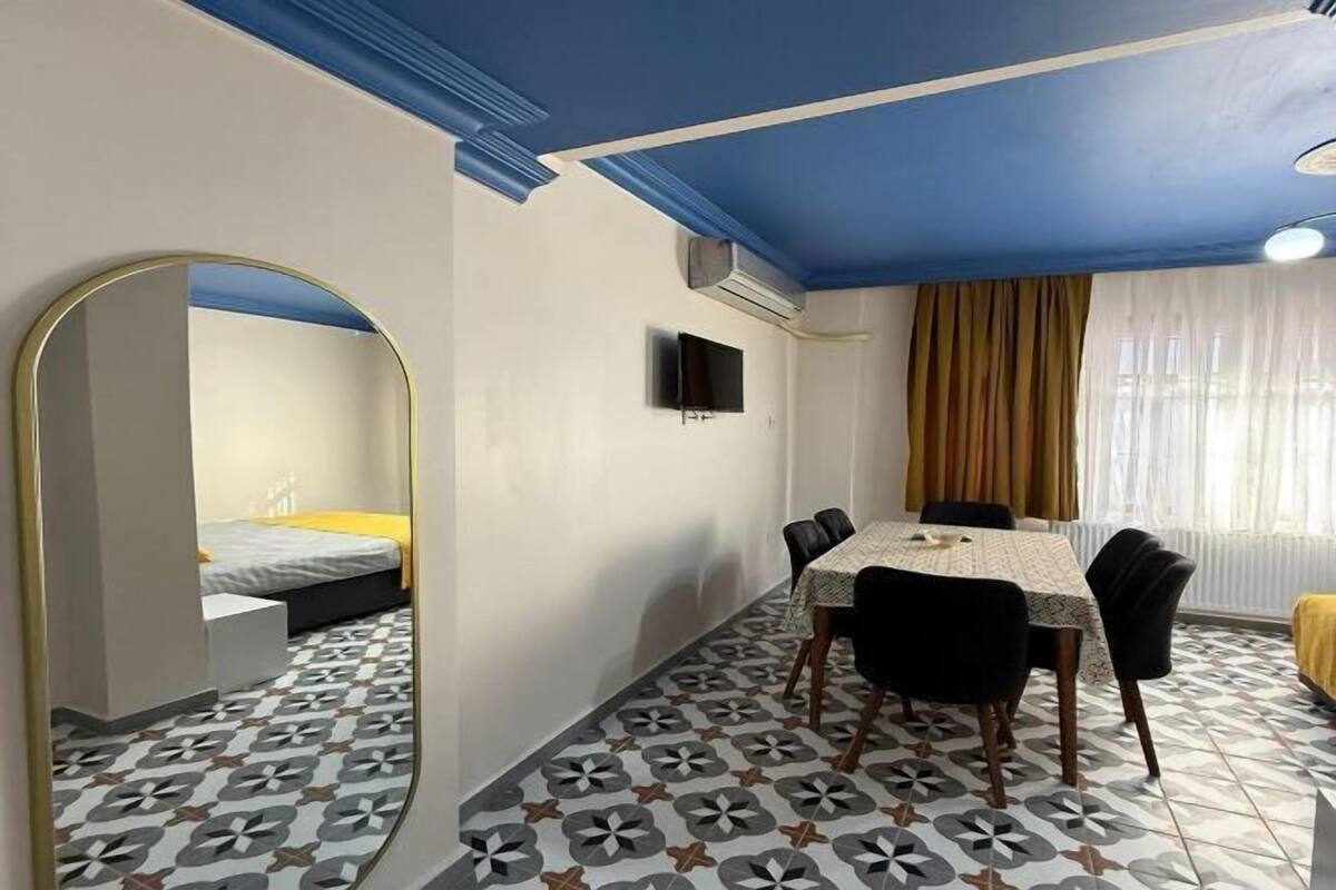 A room with a bed, a TV, a dining table with chairs, and patterned flooring.