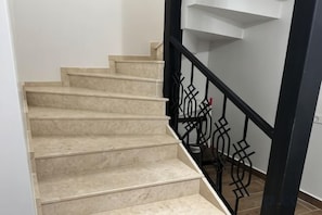 Una escalera con peldaños color beige y barandilla de metal negro.