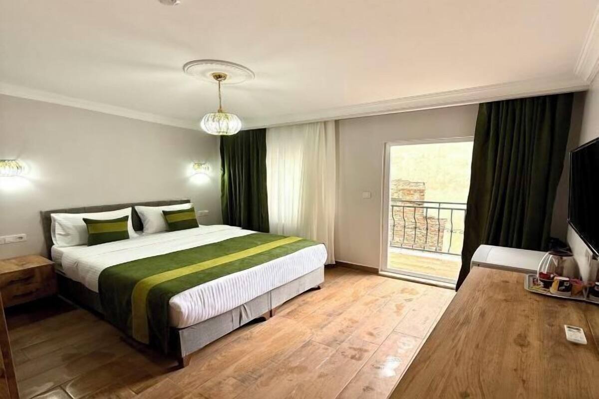 A hotel room with a bed, a wooden desk, a television, and a balcony with curtains.