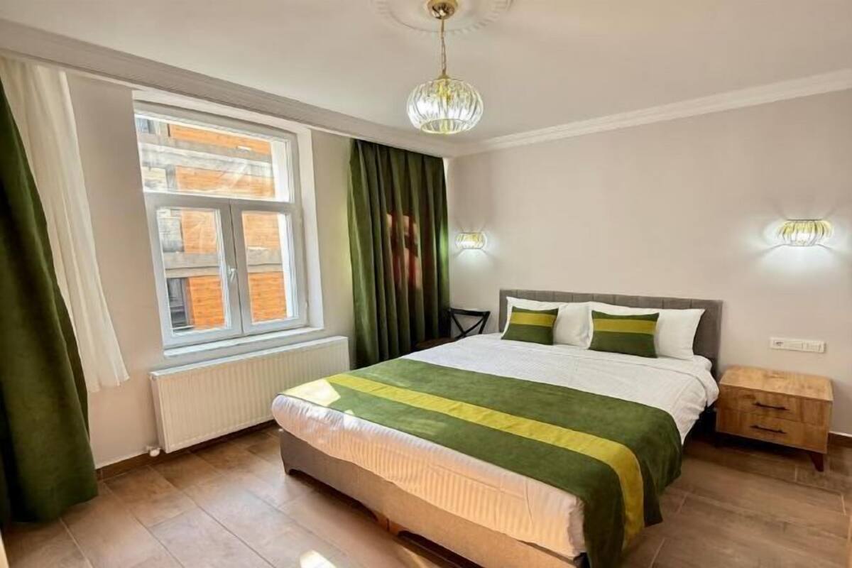 A bedroom with a large bed, a window with curtains, a radiator, and a nightstand.