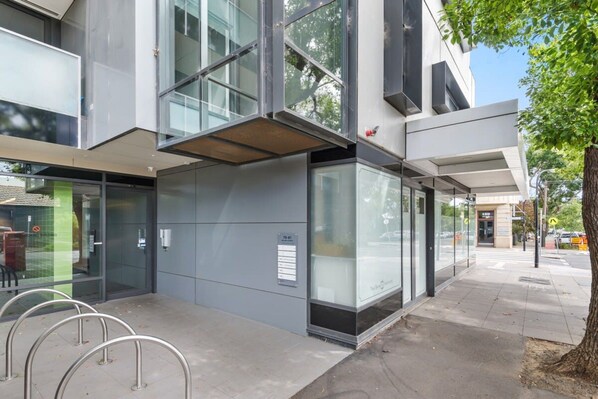 A modern building with large glass windows, metal railings, and a clear pedestrian pathway.