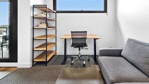 A small, modern office space with a desk, office chair, and a grey sofa. There is a bookshelf with multiple shelves and a window above the desk. - Pristine 1-bed Apartment Near Local Cafes (Melbourne)