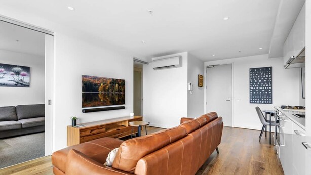 A modern living room with a brown leather sofa, a flat-screen TV, and a wooden coffee table. - Pristine 1-bed Apartment Near Local Cafes (Melbourne)