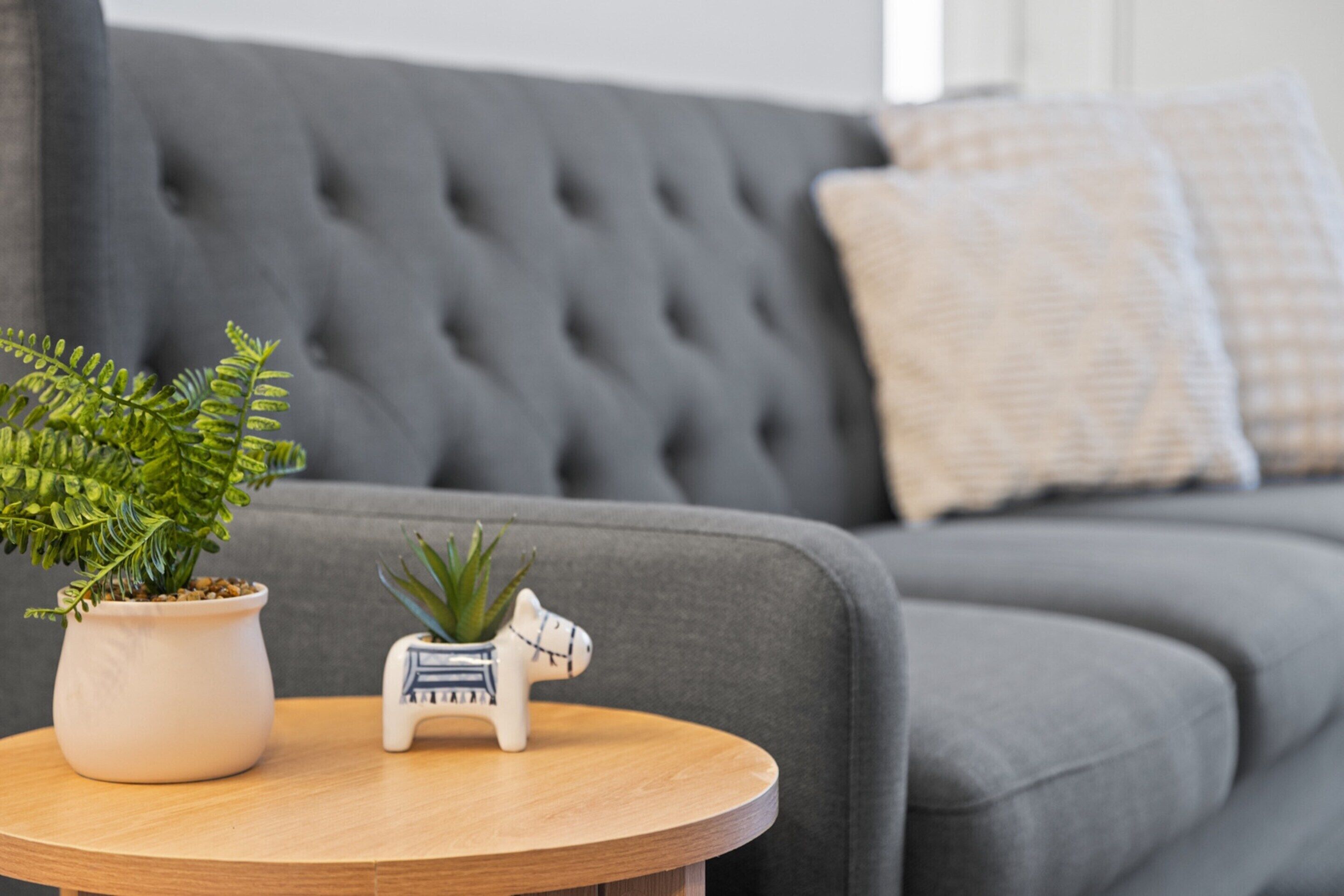 A round wooden table with a potted fern and a small white horse-shaped planter.