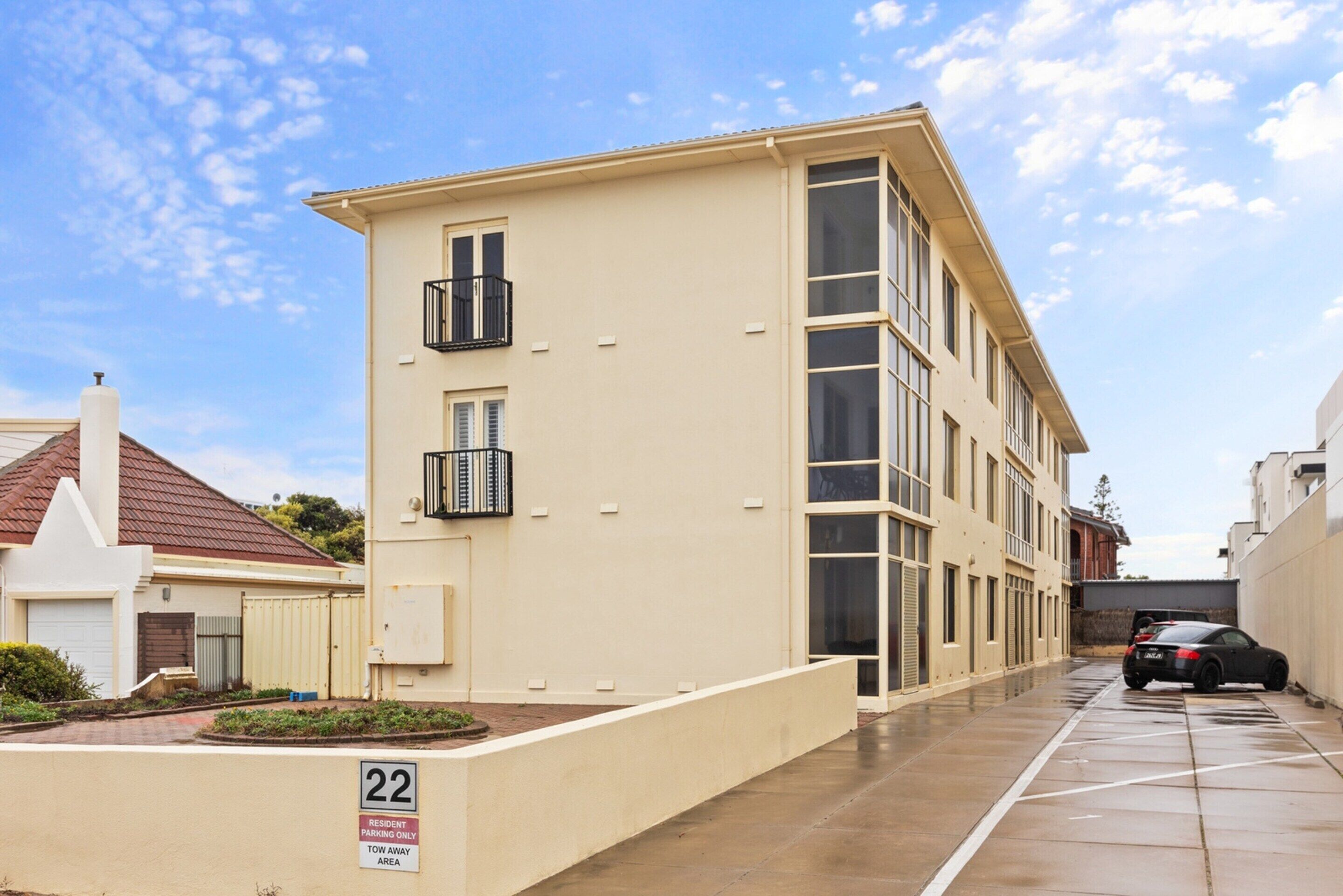 A residential building with a flat facade, a balcony, and a parking area marked with the number 22.