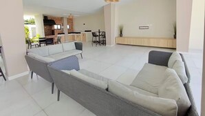 Een ruime woonkamer met een grijze bank, een eettafel met stoelen, en een keuken op de achtergrond.