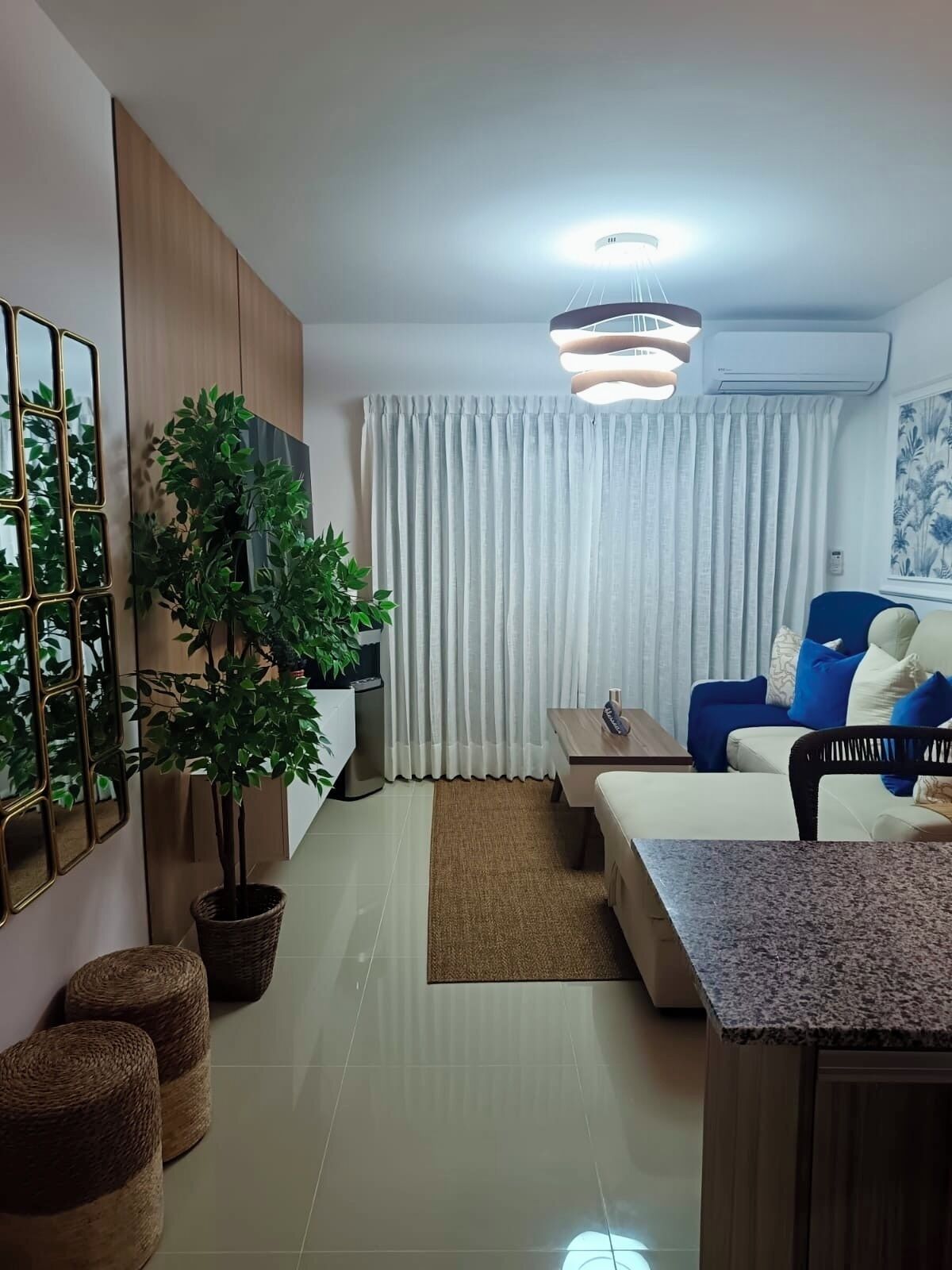 Un salon moderne comprenant un canapé, une table basse, un téléviseur, une plante en pot et un miroir décoratif.