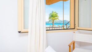 A room with a view of a beach, a wooden chair, and a bed with a white pillow. - VORAMAR 1 - Fabulous beachfront apartment. Free Wi-Fi. (Alcúdia)