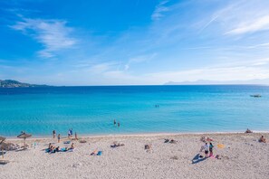 Een strand met helderblauw water, mensen die zonnebaden en parasols.