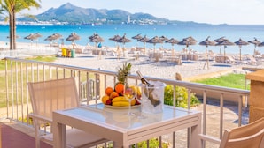 A table with a fruit bowl, a bottle of champagne, and glasses on a balcony overlooking a beach with umbrellas and lounge chairs. - VORAMAR 1 - Fabulous beachfront apartment. Free Wi-Fi. (Alcúdia)