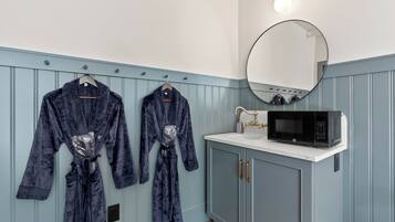 A bathroom with two robes hanging on a rack, a round mirror, and a black microwave on the counter.