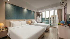 A hotel room with two beds, a large window with a view, a small table with fruit, and a wall with a leaf pattern.