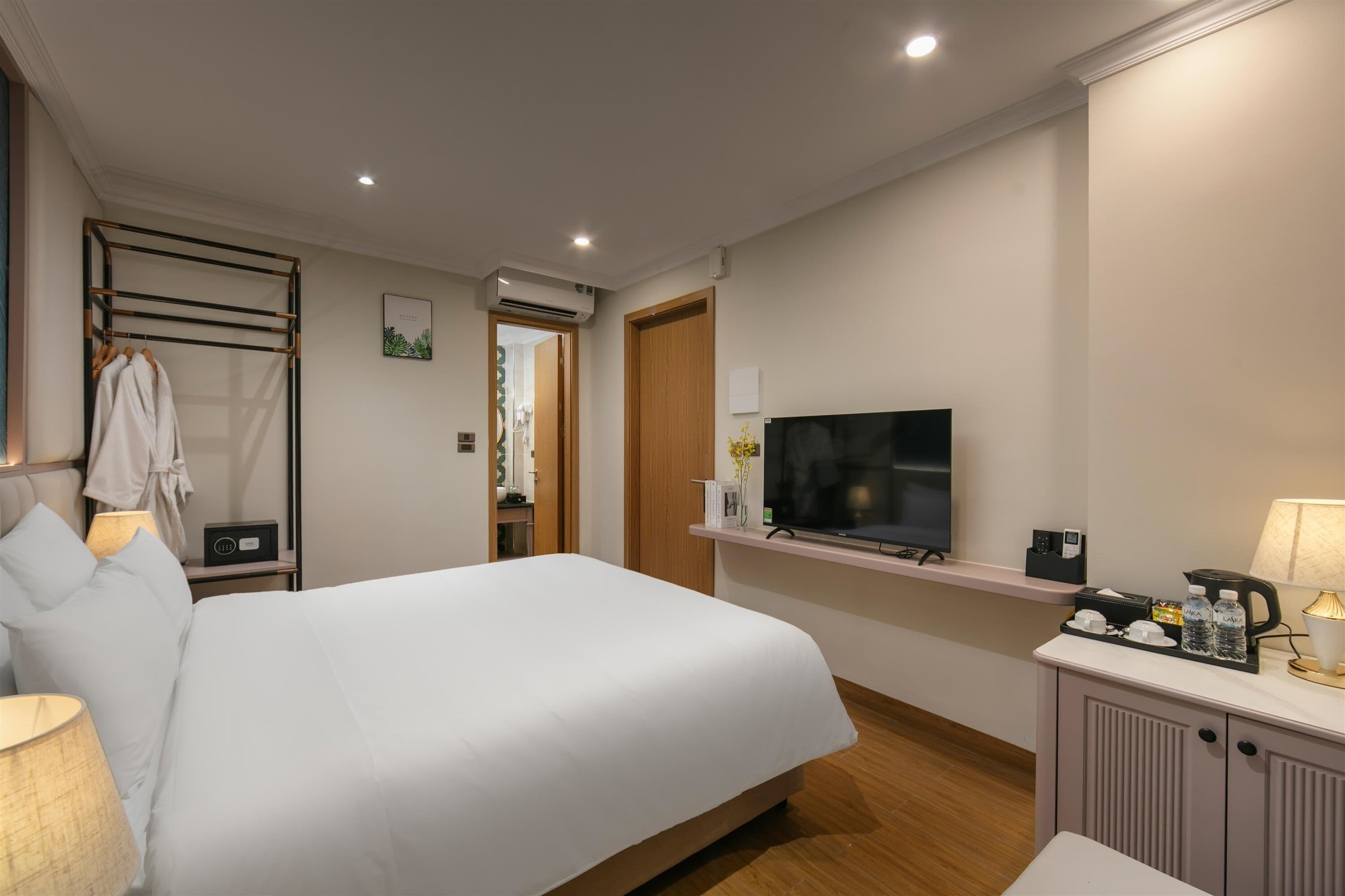 Habitación de hotel con cama, mesita de noche, televisor y una pequeña zona de kitchenette.