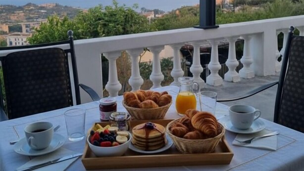 A breakfast table with croissants, pancakes, and fruit on a balcony overlooking a coastal view. - Villa with pool and terrace sea view | V02 (Imperia)