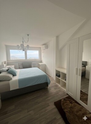 Une chambre à coucher avec un lit, un lustre, une fenêtre donnant sur un beau paysage, une armoire et une petite table.