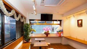 A restaurant interior with wooden benches, tables, and a large window with blinds. - Guest House Siesta (Tokyo)