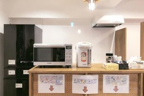 A kitchenette with a microwave, coffee maker, and a small refrigerator. There are signs with arrows on the counter. - Guest House Siesta (Tokyo)