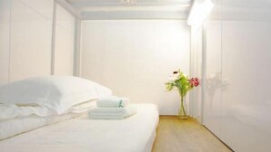 A hotel room with a neatly made bed, a small bedside table with a vase of flowers, and a wooden floor. - Guest House Siesta (Tokyo)