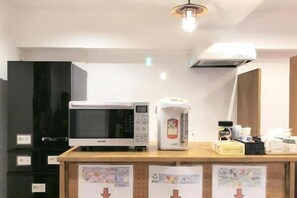 Een keukenhoek met een magnetron, rijstkoker en diverse keukenspullen op een houten aanrecht.
