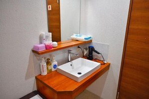 A bathroom with a white sink, wooden vanity, and a mirror. There are toiletries on the vanity and a towel rack above the sink. - Guest House Siesta (Tokyo)