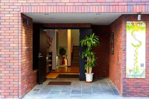 A brick building entrance with a potted plant and a poster on the wall. - Guest House Siesta (Tokyo)