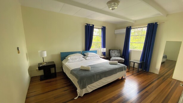 A bedroom with a large bed, a chair, a desk, and a window with curtains. - 3-bedroom Coastal Escape in lovely Christ Church with Wi-Fi, AC (Bridgetown)