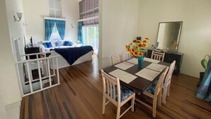 A dining area with a table set for four, a bed with blue bedding, and a window with curtains. - 3-bedroom Coastal Escape in lovely Christ Church with Wi-Fi, AC (Bridgetown)