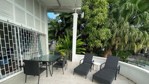 A covered patio with a glass table and chairs, surrounded by lush greenery and a white railing. - 3-bedroom Coastal Escape in lovely Christ Church with Wi-Fi, AC (Bridgetown)