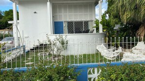 Une maison blanche à deux étages avec une porte bleue, entourée d’une clôture blanche agrémentée de touches de bleu.
