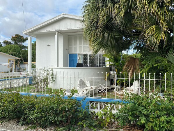 A white building with a blue door, surrounded by a white fence and lush greenery. - 3-bedroom Coastal Escape in lovely Christ Church with Wi-Fi, AC (Bridgetown)
