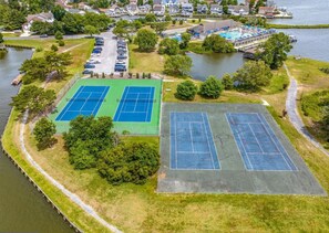 An aerial view of a lakeside property with tennis courts, a parking lot, and a boat dock.