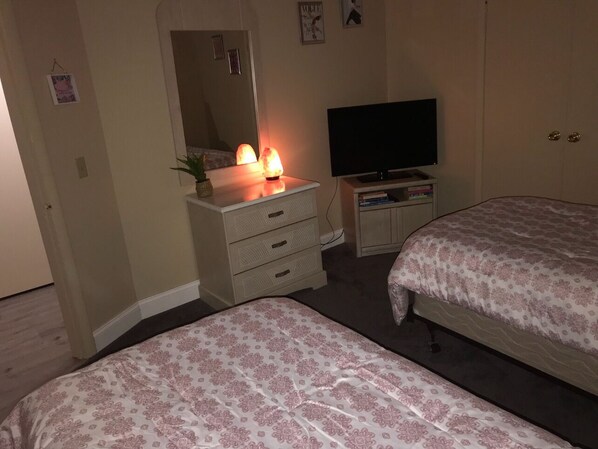 A bedroom with two beds, a dresser, a TV, and a lamp.