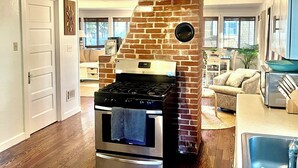 A kitchen with a brick oven, stainless steel appliances, wooden flooring, and a view to the living area. - Relaxing 3-bedroom house in Wareham by the water (Wareham)