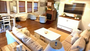 A living room with a fireplace, a television, and a dining area with a table and chairs. - Relaxing 3-bedroom house in Wareham by the water (Wareham)