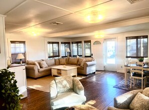 A spacious living room with a beige sofa, a patterned armchair, and a dining area with a table and chairs. - Relaxing 3-bedroom house in Wareham by the water (Wareham)