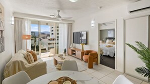 A modern living room with a sofa, coffee table, and armchairs. There is a TV mounted on the wall and a sliding glass door leading to a balcony. - Luxurious City Centre Apartment - Space & Style (Cairns City)