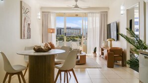 A modern living room with a dining area, a TV, and a balcony with a city view. - Luxurious City Centre Apartment - Space & Style (Cairns City)