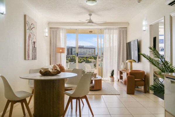 A modern living room with a dining area, a TV, and a balcony with a city view.