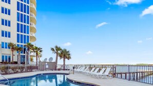 A swimming pool with lounge chairs, palm trees, and a hotel building in the background.