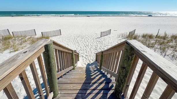 A wooden staircase leading to a sandy beach with a clear blue sky.