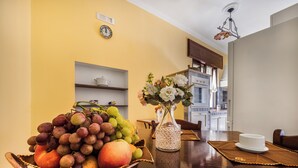 Een eethoek met een fruitschaal, een vaas met bloemen en een klok aan de muur.